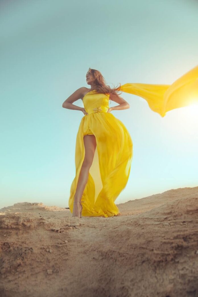 woman in yellow dress standing on brown sand during daytime