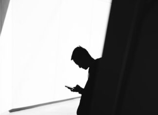 person using phone leaning on wall in silhouette photography
