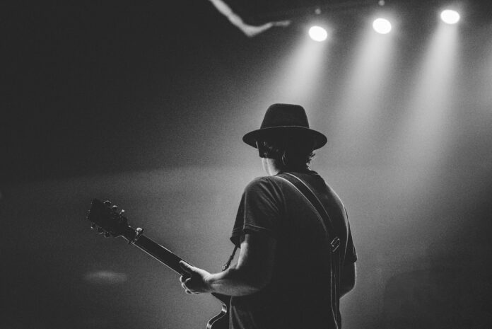 man in black t-shirt and hat playing guitar