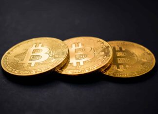 three gold-colored bitcoins on black surface