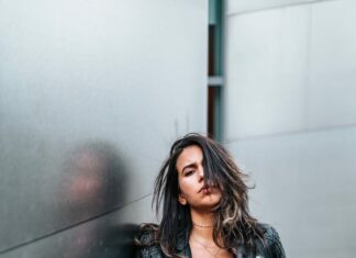 woman touching her black leather jacket while standing near silver wall