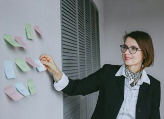 a woman in a black jacket and glasses writing on a wall