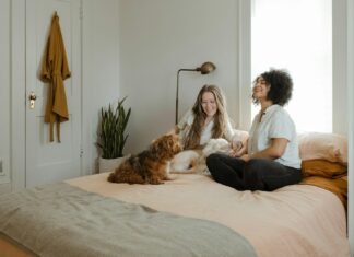 woman in white long sleeve shirt sitting on bed beside brown dog