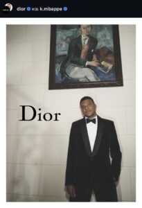 Mbappe posing in Dior under a Christian Dior portrait
